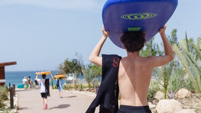 A guy carrying a surfboard on his head at Hola Surf Hostel Surf camp
