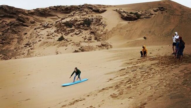Sandboarding down a sand dune with Hola Surf Hostel Surf camp