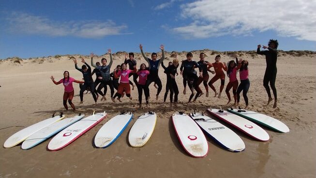 people jumping with surfboards on the beach at Shark’s Lodge surf camp in Peniche Portugal