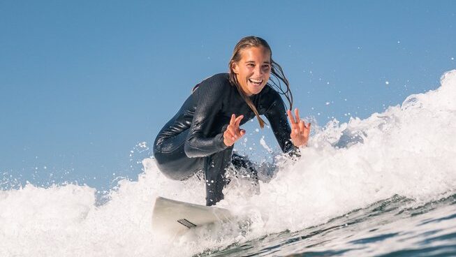 a surfer giving the peace sign with blue skies at Surf Cascais in Cascais