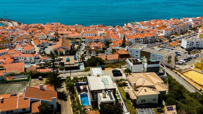 A drone shot of the salty pelican in Ericeira with red roofs and the ocean in the distance