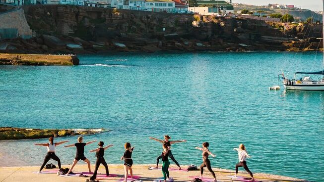 people doing yoga with a bay and headland in the background The Salty Pelican surf camp in Ericeira