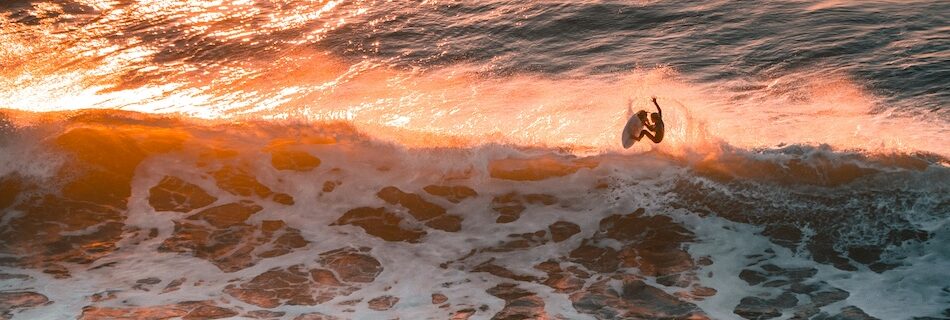 a surfer doing an aerial manoeuvre in sunlight at a surf camp Ericeira Portugal