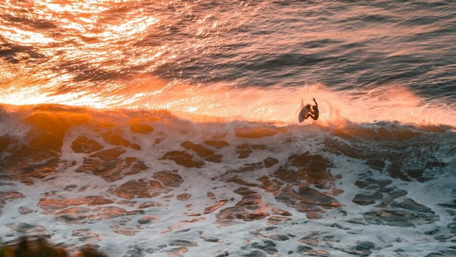 a surfer doing an aerial manoeuvre in sunlight at a surf camp Ericeira Portugal