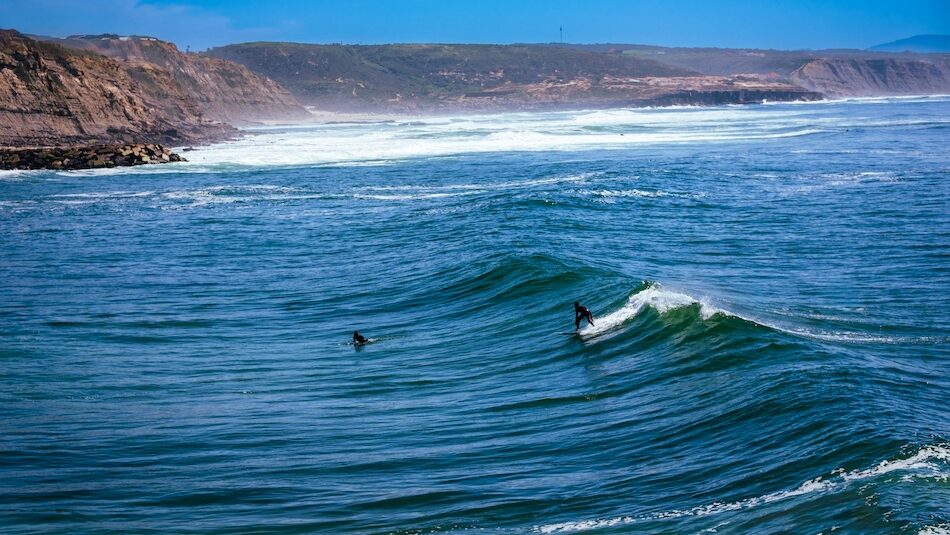 A surfer on a wave at Ericeira Portugal with blue skies and a long wave