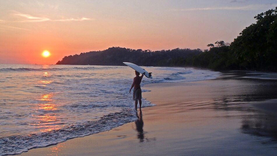 A surfer with the surfboard on his head at sun set at a surf yoga camp Costa Rica