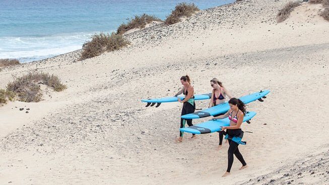 People walking down the beach with surfboards with Line Up Fuerteventura surf camp