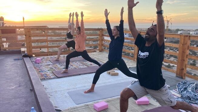People doing a yoga pose on a deck at sunset at Moana Surf Maroc surf camp