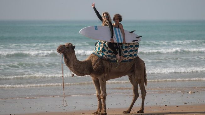A person with a surfboard on a camel at Surf & Travel Camp Morocco surf camp