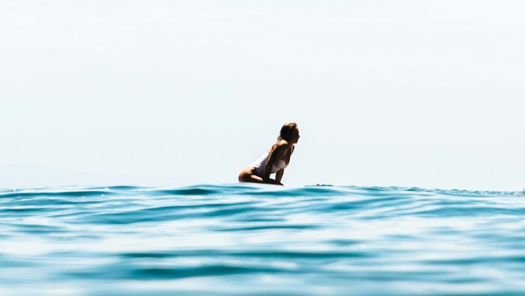 A girl sitting on a surfboard in blue water at a affordable surf camps Sri Lanka