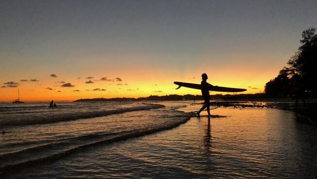 sunset at weligama with a person holding a surfboard