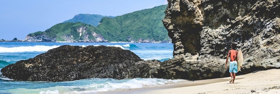 A surfer walking on sand to the water during his Indonesia surf camp experience