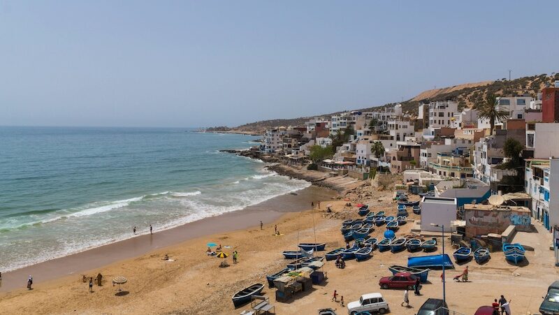Are Surf Camps In Morocco Safe? My Honest Experience After Two Trips The town of Taghazout and the ocean showing why are surf camps in Morocco safe and welcoming