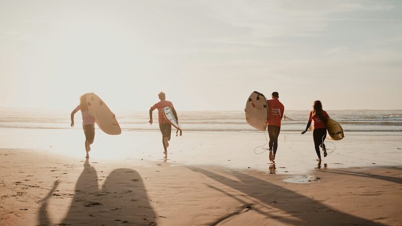 A group of surfers walking into the surf with the sun and wondering is a surf camp worth it