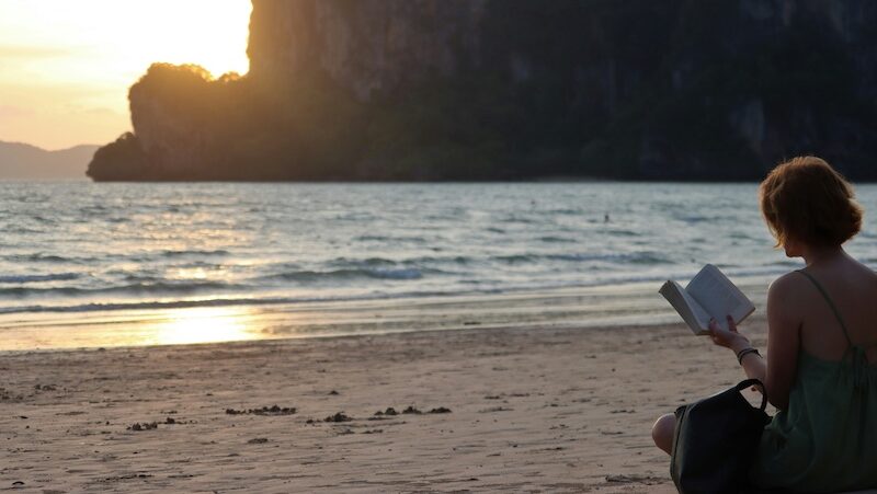 A solo traveller reading a book on the beach