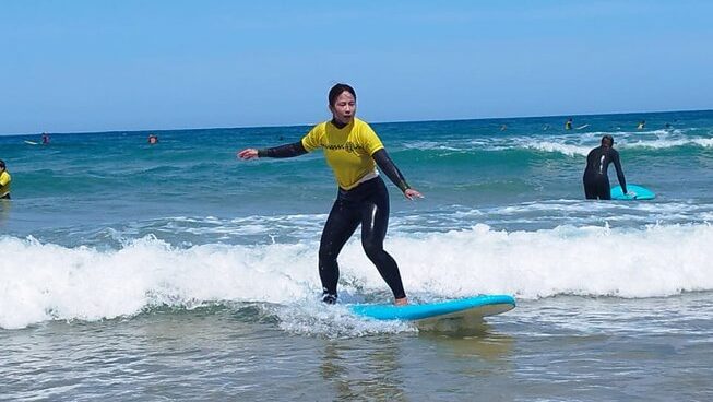 learner surfers catching a wave in blue water and skies at a surf hostel Peniche