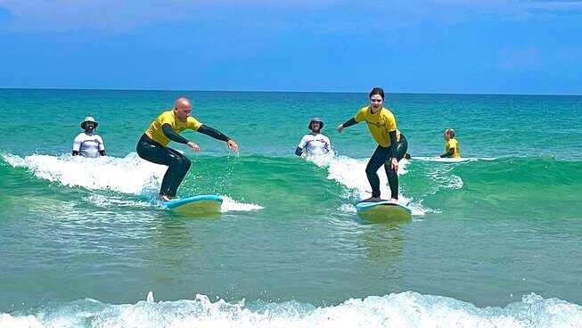 learner surfers catching a wave in blue water and skies at a surf hostel Peniche