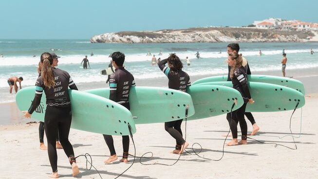 Learner surfers carrying surfboards into the water at a surf hostel Peniche