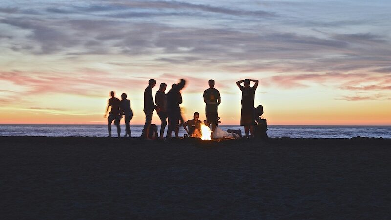 People around a camp fire on the beach with the sun setting