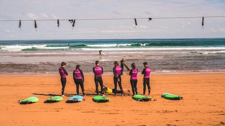 a group of people listening to a surf instructor on the beach with the ocean