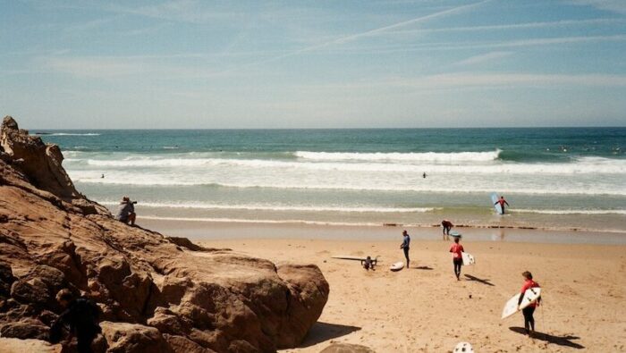 learner surfers walking into the ocean with surfboards thinking Where to surf in Portugal in summer
