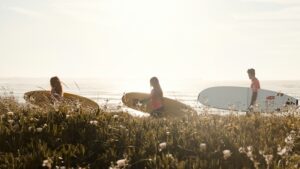 3 people walking with surfboards with the sun behind them thinking Where to surf in Portugal in summer