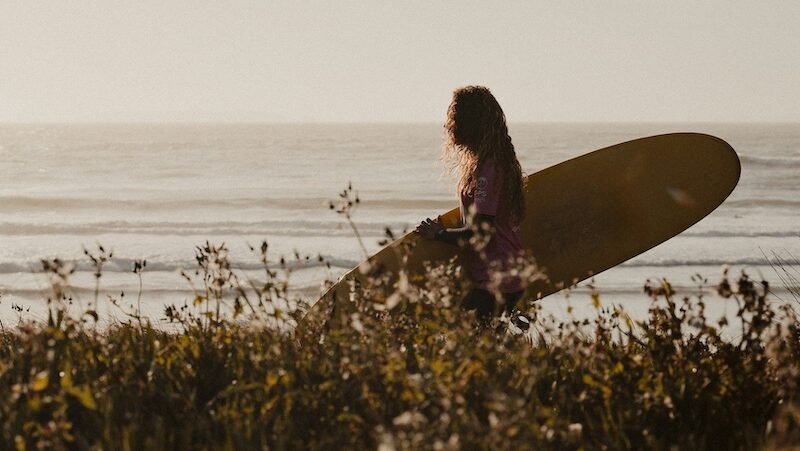 1 person with their surfboard in Peniche walking and thinking Where to surf in Portugal in summer