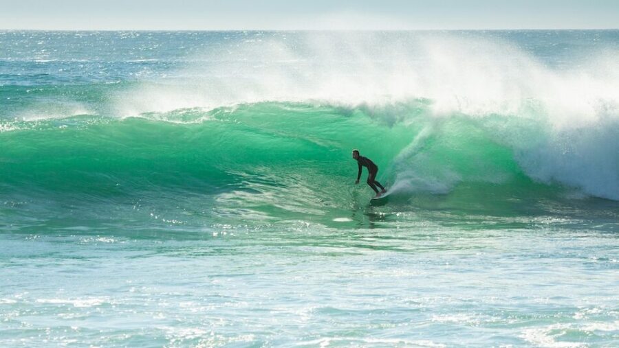 A surfer on a bright blue wave and not thinking when is the best time to surf Portugal