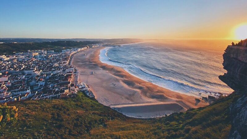 Portugal surf at sunset with the town and beach and people thinking when is the best time to surf Portugal