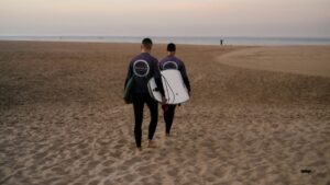 Two surfers carrying surfboards to the water when looking for Portugal vs Morocco Surf Camps