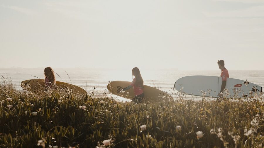 Surfers walking to the ocean all behind each other with the sun at Portugal