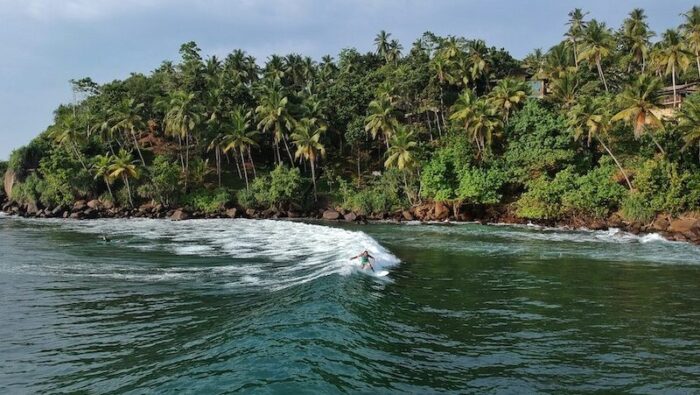 A surfer on a wave in Mirissa Sri Lanka with forest