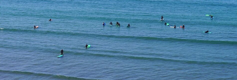 surfers in the water who were once wondering Tamraght vs Taghazout Beginner Surf Comparison